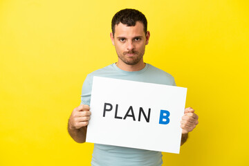 Brazilian man over isolated purple background holding a placard with the message PLAN B with sad expression