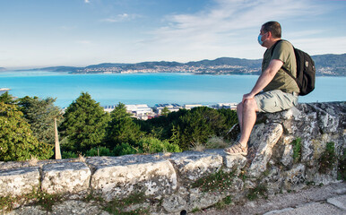 Hombre con mascarilla y mochila observando la desembocadura de la ría de Vigo desde el castillo...