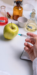 Food specialist injects a chemical into a green apple with a syringe. Food quality. Vertical format.