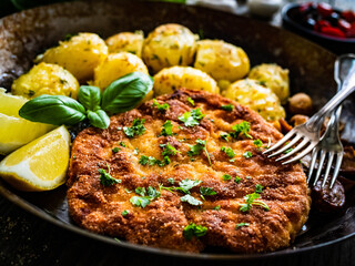 Breaded fried pork chop, potatoes and white mushrooms on wooden table 