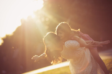 Mother and daughter playing in nature. Mom carrying kid on piggyback.