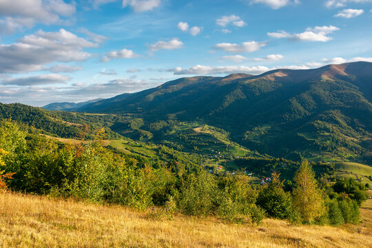 rural landscape in evening light. beautiful countryside scenery of carpathian mountains. trees, fields and meadows on the hills. village down in the distant valley. september sky with fluffy clouds