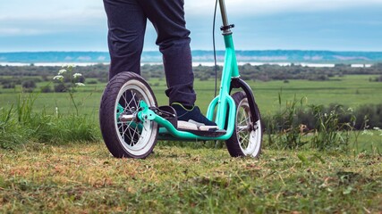 Child's feet on a scooter with large wheels among the green grass. Active lifestyle © Aleksandr 44ARH