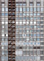 The facade of an old city hostel with rusty fire escape and different air conditioners