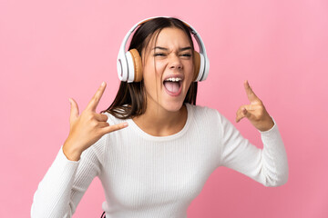 Fototapeta premium Teenager girl isolated on blue background listening music making rock gesture