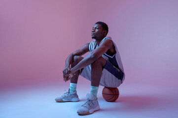 Basketball player sitting on ball in studio