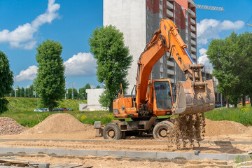 Wheeled backhoe loader with a bucket pours sand into the space for the future sidewalk. Construction of a pedestrian street. Work on laying paving slabs. Heavy machinery