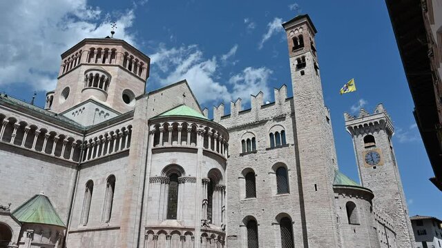 Trento, Trentino, Italy, June 2021. On a beautiful summer day nice pan footage of the San Vigilio Cathedral rear three quarters. Next to it the bell tower surmounted by a yellow flag.