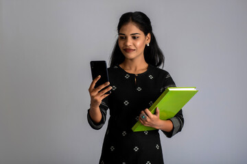 Pretty young girl holding book and using mobile on grey background