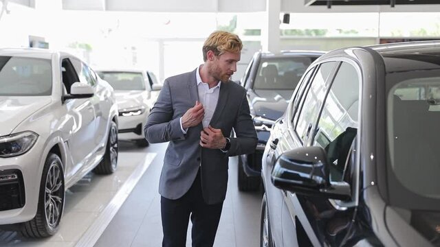 Happy adult man customer male buyer businessman client wears classic suit chooses auto wants to buy new automobile in car showroom vehicle salon dealership store motor show indoors. Car sales concept