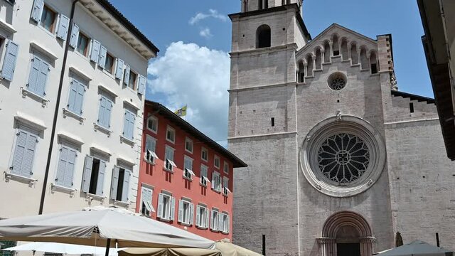 Trento, Trentino, Italy, June 2021. On a beautiful summer day tilt footage of the facade of the Cathedral of San Vigilio. In evidence the large rose window. People passing by.