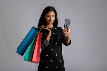 Portrait of a young woman using mobile phone with shopping bags in her hands.