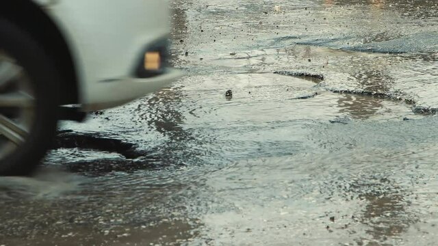 Large potholes after rain, badly damaged road infrastructure. Close-up of cars driving slowly along the road with pits and puddles. Asphalt in violation of technology. Taxpayer money is wasted. UHD 4K