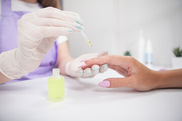 Professional manicurist applying cuticle oil on fingers of female client