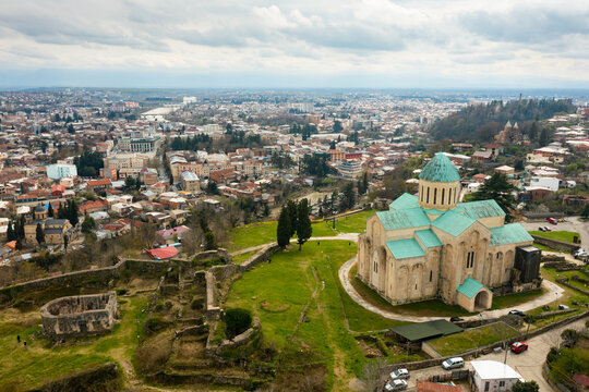 View from drone of impressive rebuilt building of Cathedral of Dormition, temple of Georgian Orthodox Church in Kutaisi against cityscape in springtime.