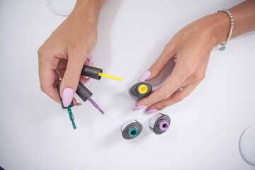 Top view close up of female hands holding colorful nail gel bottles