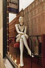 Obraz na płótnie Canvas white plastic dummy woman sits in shop window under bus stop sign in city