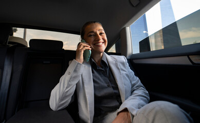 Working in a taxi. Side view of a successful businesswoman using smartphone while sitting on the back seat in the car