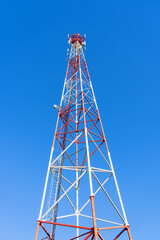 A bottom view of the cell tower. Red and white metal structure against a clear blue sky....