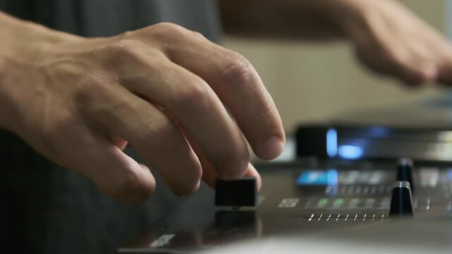 Hand of hip hop dj playing music. Disc jockey adjusting cross fader knob on sound mixer while scratching vinyl record disc on turn table player device, filmed in slow motion video clip in closeup