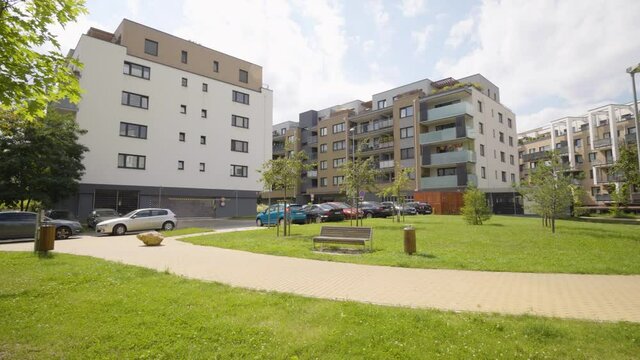 An apartment complex with a walkway, greenery and a parking lot in a suburban area