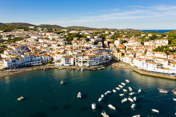 Naklejka na ściany i meble Scenic aerial view of Cadaques shoreline overlooking white buildings and boats parked in bay in summer, Catalonia, Spain