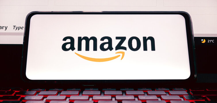 Amazon. A logo da Amazon na tela de um celular que est&aacute; sobre um teclado de notebook com ilumina&ccedil;&atilde;o de leds. Fotografia em ambiente noturno. Site, Com&eacute;rcio eletr&ocirc;nico, online, Venda, Varejo, produto.