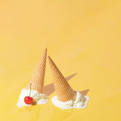 Creative layout with two ice cream cones up side down and vanilla ice cream scoops with red cherry on bright yellow background. Summer dessert and fruit aesthetic idea. Trendy food lay out.