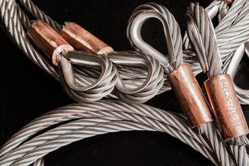 Stainless steel cable, with loops and copper clamps, and a black background, close-up.