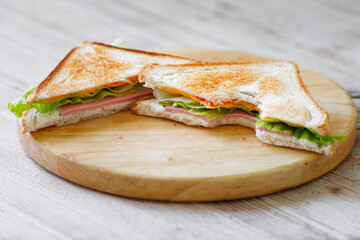 The cut sandwich lies on a wooden board on the table. Breakfast