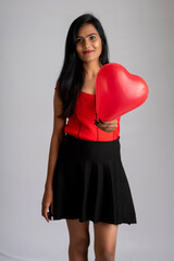 Cheerful cute girl in fancy red and black outfit posing with heart shape balloon.