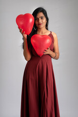 Cheerful cute girl in fancy red outfit posing with heart shape balloon on grey background