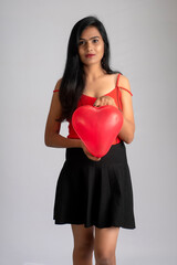 Cheerful cute girl in fancy red and black outfit posing with heart shape balloon.