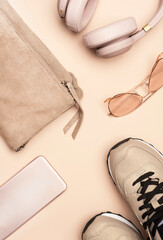 Girls hipster summer nude pink stuff and accessories: bag, sneakers, phone, headphones, sunglasses on pale pink background, top view