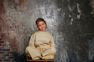 Cute little girl sitting on a chair on the gray background. Space for text.