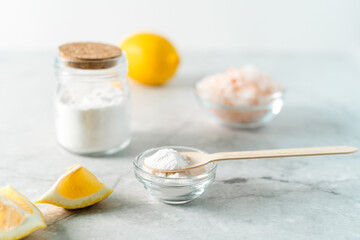 Eco friendly natural cleaners, jar with baking soda, lemon, pink salt and wooden spoon on marble table background. Organic ingredients for homemade cleaning. Zero waste concept.