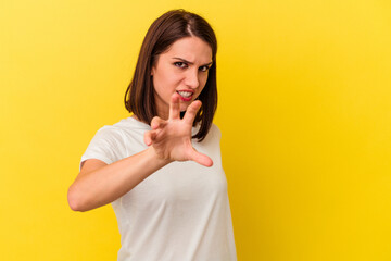 Young caucasian woman isolated on yellow background showing claws imitating a cat, aggressive gesture.