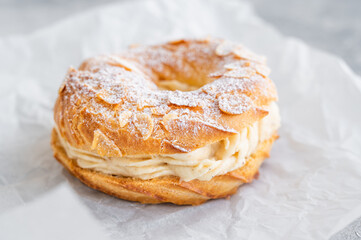 French traditional cake Paris Brest with praline cream, powdered sugar and almond petals on top on a gray concrete background. Copy space.