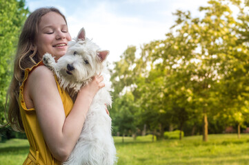 Portrait of a happy teenage girl with her white terrier dog in the summer in the park