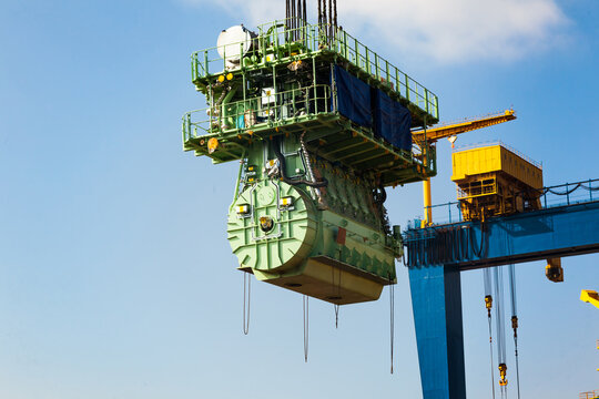 Transportation of a large marine engine by a port crane using steel cables.