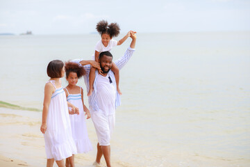 Happy African american family holding hands and walking together on the beach during holiday.