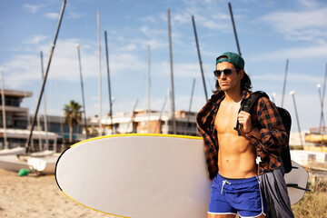 Portrait of handsome surfer with his surfboard. Young man with a surfboard on the beach