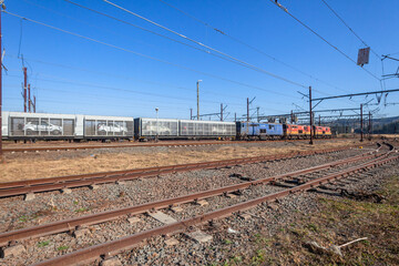 Fototapeta na wymiar Train Locomotives Transporting New Car Vehicles in Cargo Carriers on Rail Track Networks