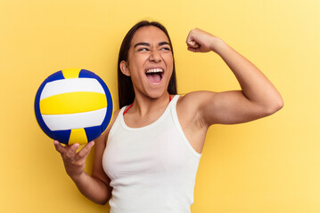 Young mixed race woman playing volleyball on the beach isolated on yellow background raising fist after a victory, winner concept.