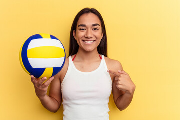 Young mixed race woman playing volleyball on the beach isolated on yellow background person pointing by hand to a shirt copy space, proud and confident