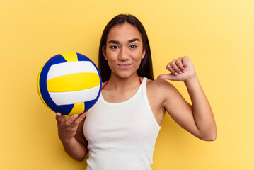 Young mixed race woman playing volleyball on the beach isolated on yellow background feels proud and self confident, example to follow.