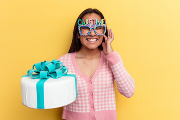 Young mixed race woman holding a cake isolated on yellow background covering ears with hands.