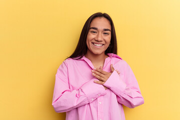 Young mixed race woman isolated on yellow background has friendly expression, pressing palm to chest. Love concept.