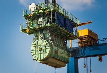 Transportation of a large marine engine by a port crane using steel cables.