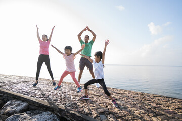 asian parent and children jumping up and down sport. healthy family stretching and exercise in the...